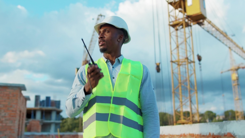 African american man builder engineer worker in hard hat with use a walkie-talkie on construction helmet industrial site industry structure architecture inspector builder slow motion Royalty-Free Stock Footage #1059264623