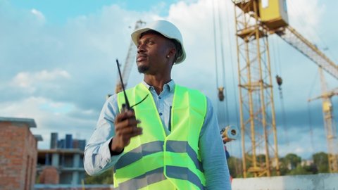 African american man builder engineer worker in hard hat with use a walkie-talkie on construction helmet industrial site industry structure architecture inspector builder slow motion