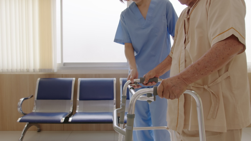 Close up attractive young asian woman or nurse take care senior old man on cane or walker feeling helpful and empathy at nursing home or hospital hallway. Hip, knee and leg problem in older people.