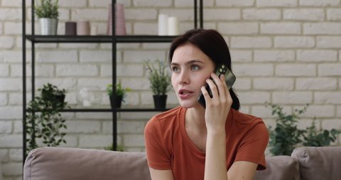Young woman makes appointment by phone while sit on couch at home. Client receive consultation distantly, informal pleasant conversation with friend, communication using modern wireless tech concept
