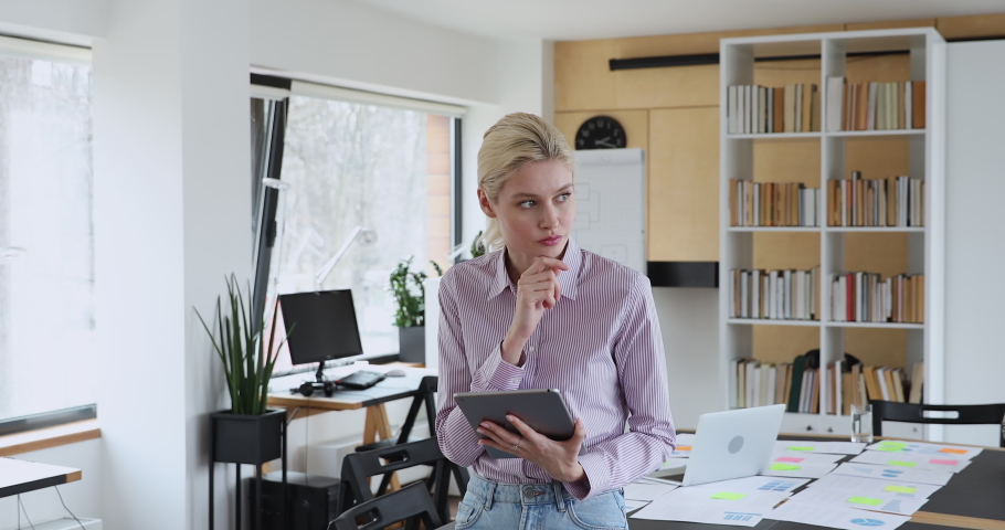Pretty thoughtful serious young blond female employee company ceo business woman standing in office holding tablet device working, thinking, search problem solution, ideas, lost in thoughts concept Royalty-Free Stock Footage #1059268139