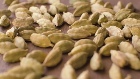 Macro shot of green dried cardamom seeds - famous aromatic spice - on the wooden background. Extreme close up, camera slowly moving on slider