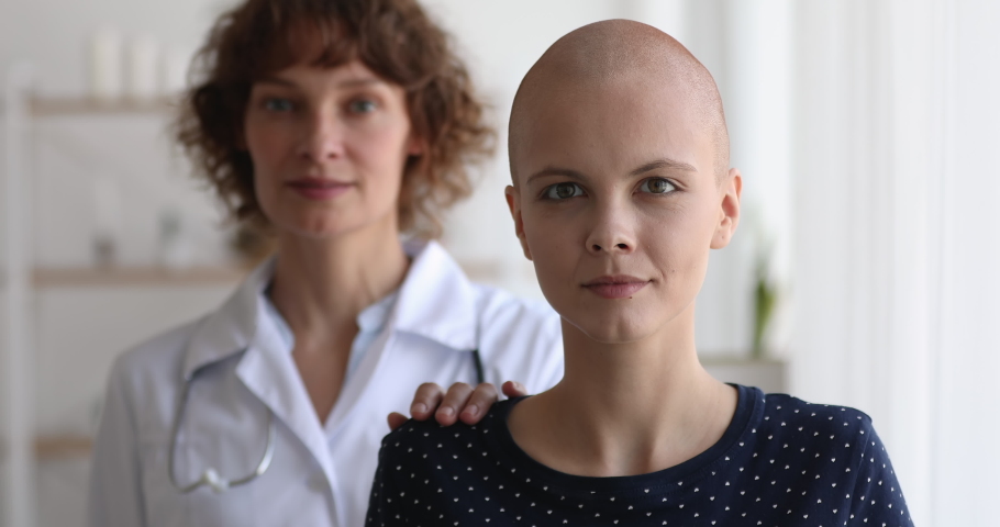 Middle-aged woman oncology nurse practitioner standing behind cancer patient, smile look at camera, head shot portrait. Doctor supporting ill female put hand on shoulder as symbol of help and Royalty-Free Stock Footage #1059269936