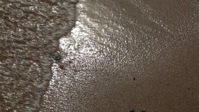 Top view of motion of sea waves over golden sand in a summer day.