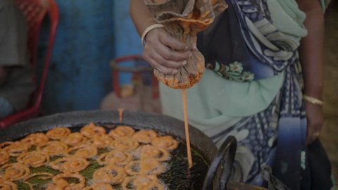 Woman in a dress making traditional sweet orange jalebi snacks on a street food market in central India in slowmotion