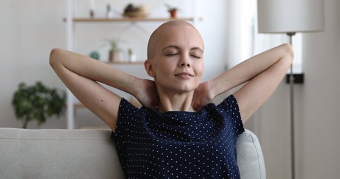 Bald-headed female closed eyes put hands behind head relaxing lean on sofa daydreams enjoy fresh air and new day. No stress, fatigue relieve, cancer disease woman dream about recovery feel alive
