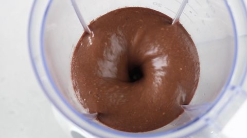 Making chocolate protein smoothie or milkshake. Closeup view of chocolate smoothie blending in a mixer in slow motion