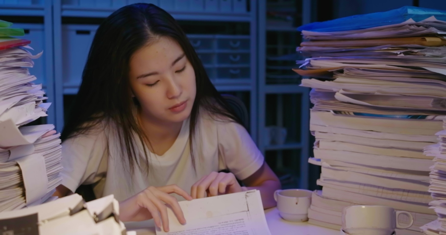 Unhappy young asian student woman is sitting at desk cover with stack of paperwork and mess of her hair. Alone teen girl exhausted, tired and sighting in frustration while studying hard at late night. Royalty-Free Stock Footage #1059280412
