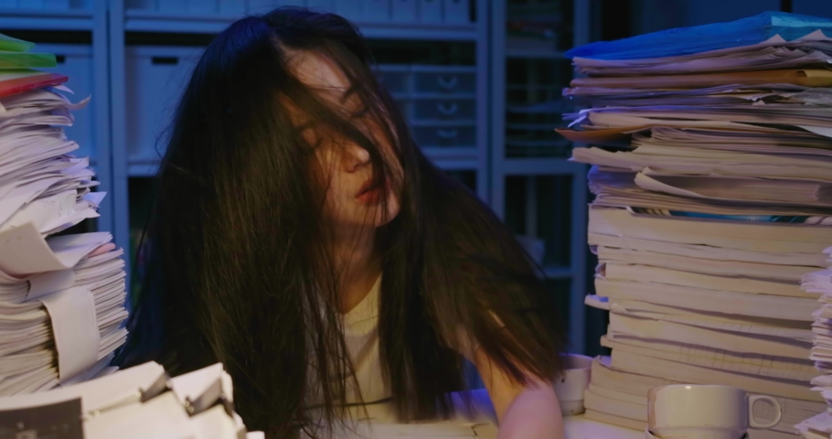 Unhappy young asian student woman is sitting at desk cover with stack of paperwork and mess of her hair. Alone teen girl exhausted, tired and sighting in frustration while studying hard at late night. | Shutterstock HD Video #1059280412
