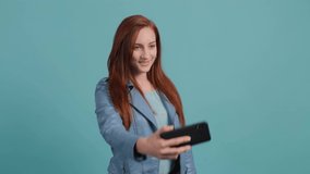 Funny young red haired woman making selfie on a turquoise background.