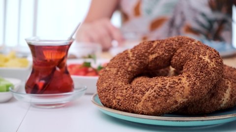 A person out of the depth of field is having breakfast, prepared a traditional Turkish breakfast with simit and tea in focus.