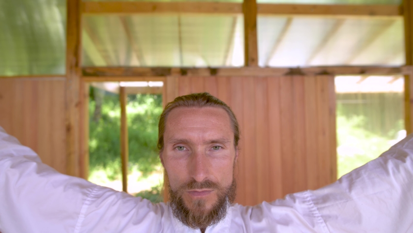 Bearded caucasian man wearing white clothes to practice concentration and breathing before practicing qigong tai chi