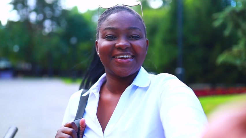 Beautiful smiling young african woman wearing white t-shirt and holding a copybook backpack and making selfie