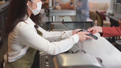 Customer use dummy credit card for purchase without touching EDC to female staff wearing surgical mask in cafe to keep distancing during COVID pandemic. Cashless, technology, wireless payment concept.