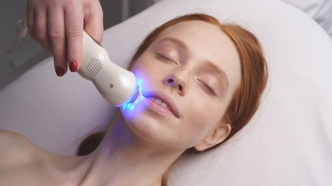 cosmetologist moves the manipulator with a cooling blue light over the skin of the face. Hardware cosmetology.