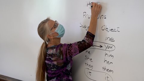Closeup portrait of smiling mature woman english grammar teacher, set against a white board in a school classroom.