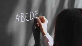 Elementary primary school girl pupil holding chalk writing on blackboard. Child preteen schoolgirl learning english alphabet letters handwriting standing in classroom. Close up back view. - Powered by Shutterstock - Get 15% off with code: PIKWIZARD15