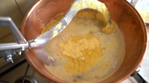 Traditional preparation of italian yellow polenta in copper cauldron with stirring metal whisk, corn flour mixing with boiling water, hot maize porridge is a typical dish of northern Italy. Italian