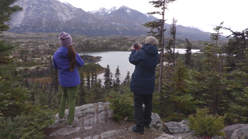 Yukon landscape with People hiking on travel living outdoor lifestyle. Travelers on hike taking photos at mountains landscape in autumn. Tourists from Alaska cruise ship excursion.
