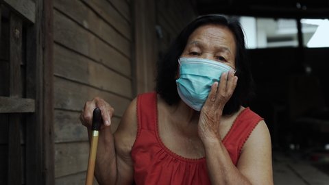 Thai elderly woman in round-necked sleeveless collar wearing medical mask for protect corona virus (covid-19) pandemic in old wooden home