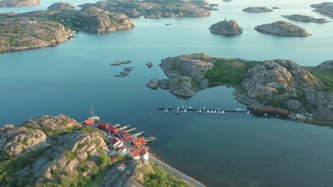 Small harbor at sunset in Swedish archipelago on the west coast of Sweden. Granite rocky islands from above in aerial drone shot. Red cabin cottages or fishing houses at shoreline. Boats in bay