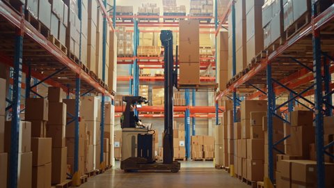 Retail Warehouse full of Shelves with Goods: Electric Forklift Truck Operator Lifting Pallet with Cardboard Box on a Shelf. Working in Logistics Storehouse Product Logistics and Delivery Center