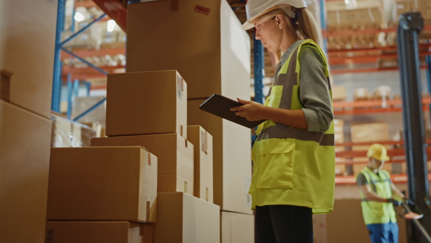 Retail Warehouse full of Shelves with Goods in Cardboard Boxes, Female Worker Scans and Sorts Packages for Delivery. Loaders Move Products with Pallet Trucks. Distribution Logistics Center. Low Angle | Shutterstock HD Video #1059312650