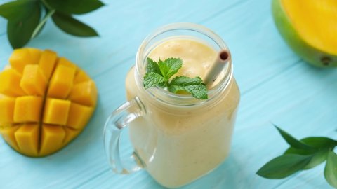 Serving jar of delicious tropical mango smoothie with bamboo drinking straw. Blue wooden background. Healthy vegetarian smoothie