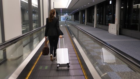 Woman walk on travelator at empty passage of modern airport. Late flight arrive to destination, no other passengers seen around. Moving camera follow behind