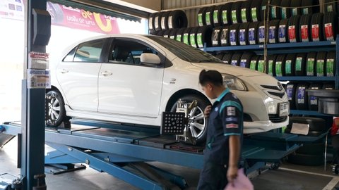 Mechanic Check Wheel Balancing of Lifting Car with Special Equipment, Signs Papers at Service Station. Man Diagnosis Car with Sensor on Wheel to Check Alignment Camber Toe. Bangkok, Thailand, Feb 2020