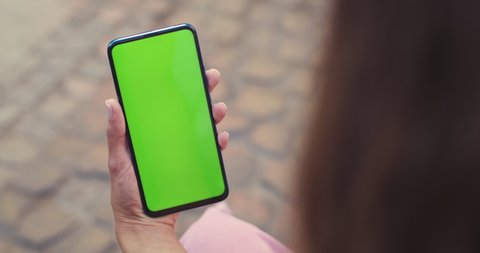 Over shoulder view of female person holding smartphone with mockup screen while sitting at street. Concept of chroma key and greenscreen