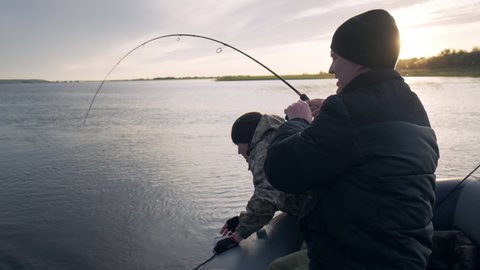 Friends fishing. Two amateur anglers fishing from the boat and fighting with trophy fish