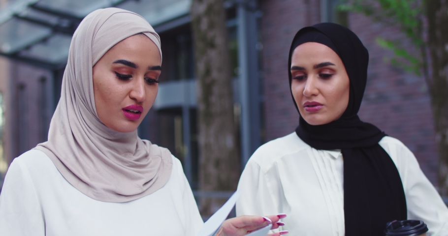 Close up of two Aribic business women in traditional headscarves walking and discussing documents talking, drinking coffe. Professional coworkers discussing cooperation. Teamwork, business, lifestyle. | Shutterstock HD Video #1059330776