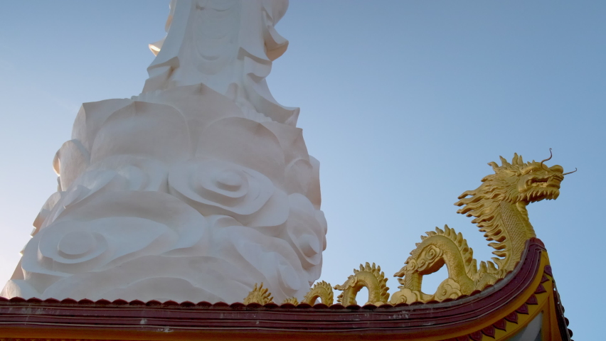 Low angle shot of white Buddha statue with golden dragons at the bottom. Buddhism religion. Ho Quoc Pagoda in Phu Quoc, Vietnam