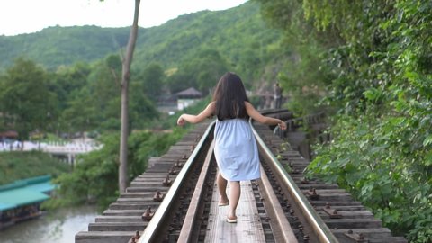back of asian child or kid girl walking on death railway or traditional train tracks and railroad in platform station to play balance or fear height for holiday relax and vacation travel transport