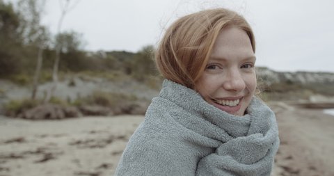 Pretty female at the beach looking at camera wrapped in towel after swim in Autumn