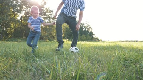 Happy family playing in the Park dad and son playing with a soccer ball. A child runs through the green grass, kicking a ball. Teamwork in the family of father and son. Children's dreams of sporting