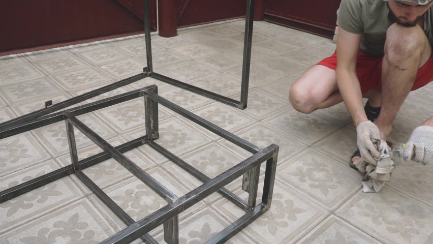 Young man in work uniform and gloves wipes the metal frame