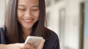 A smiling and laughing Asian teenage girl enjoy funny social media on her mobile phone.
