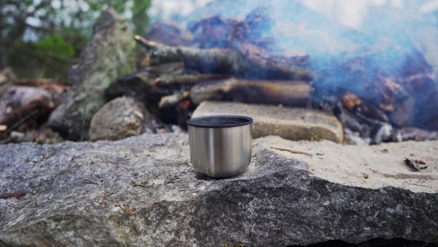 Metal mug with hot tea front of campfire. Slow motion footage. | Shutterstock HD Video #1059345680