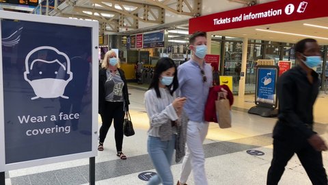 London / United Kingdom - September 21, 2020: Commuters walk next to a sign warning people to wear a face covering due to Coronavirus, COVID-19 pandemic, in Liverpool street station, central London.