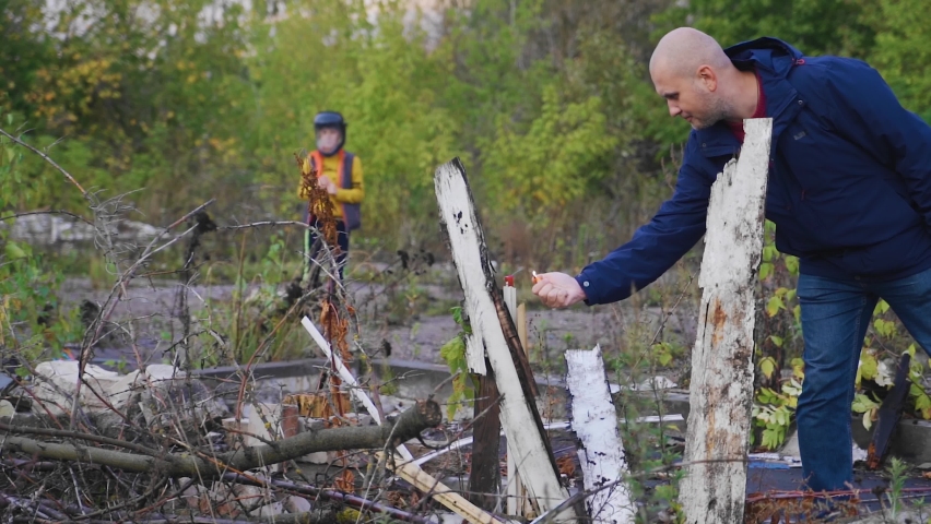 The father sets fire to the firecracker and the son in a protective helmet watches the explosion.