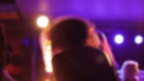 Blurred video of a girl with loose hair dancing on the dance floor in front of the stage with yellow spotlights in the background.