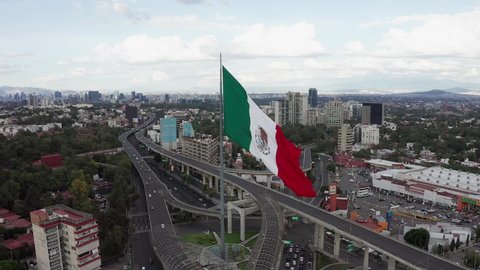 Mexico City / Mexico - 09 21 2020: Circle flight by large majestic patriotic red, white and green Mexican flag waving in wind above Periferico sur street in downtown Mexico city center, San Jeronimo, 