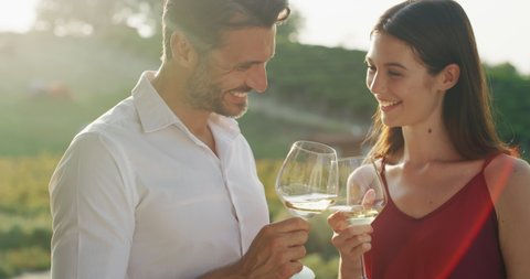 Authentic shot of happy couple in love is enjoying romantic date and cheering with white wine glasses to celebrate their anniversary and timeless love on scenic vineyards background.