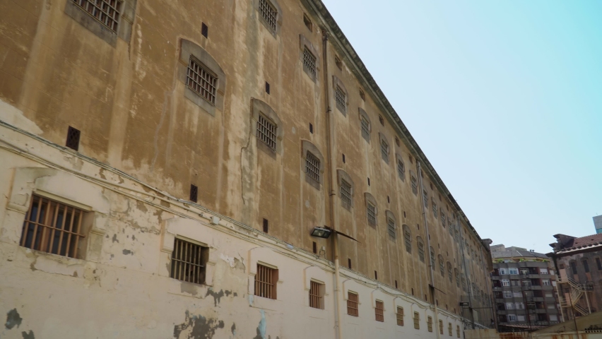 Old shabby prison wall with rusty metal jail bars on windows. Blue sky background. Between isolation and freedom concept Royalty-Free Stock Footage #1059375206