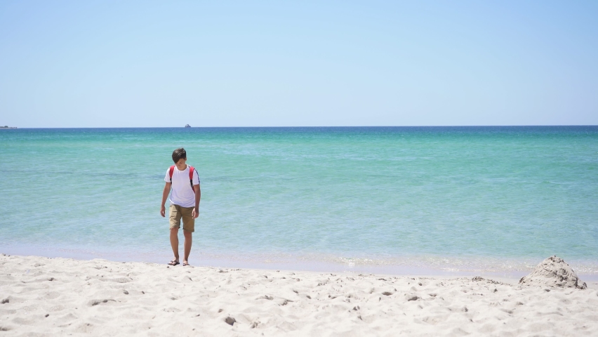 Teenager on the background of the azure sea walks along the beach on a Sunny summer day. He