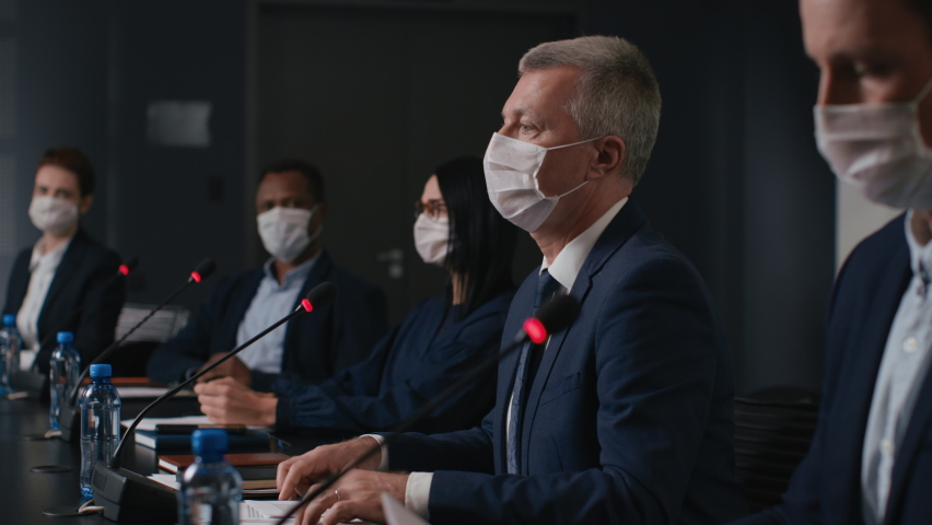 Speech of political speaker at meeting room of business forum. Man in suit and mask discusses covid-19 pandemic. 2019-ncov conference indoors of convention hall. Expert group works at official event Royalty-Free Stock Footage #1059381563