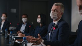 Speech of political speaker at meeting room of business forum. Man in suit and mask discusses covid-19 pandemic. 2019-ncov conference indoors of convention hall. Expert group works at official event - Powered by Shutterstock - Get 15% off with code: PIKWIZARD15