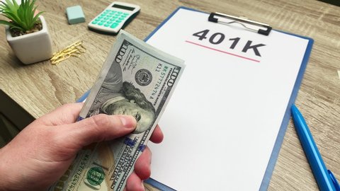 401k retirement plan, a man counts 100 dollar bills at a wooden table.